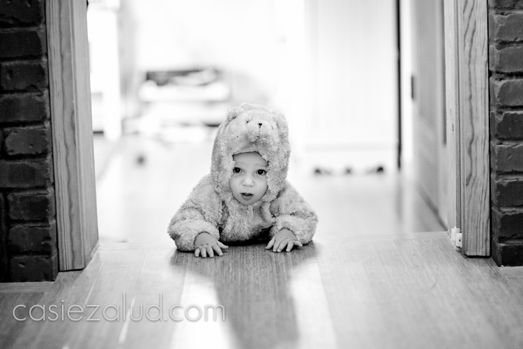 a ten month old little boy crawling in a bear costume towards a door jam on wood floor