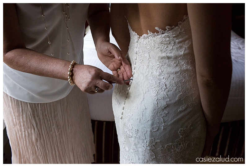 Mother using a knitting needle to put on all the button loops of her daughter's wedding dress