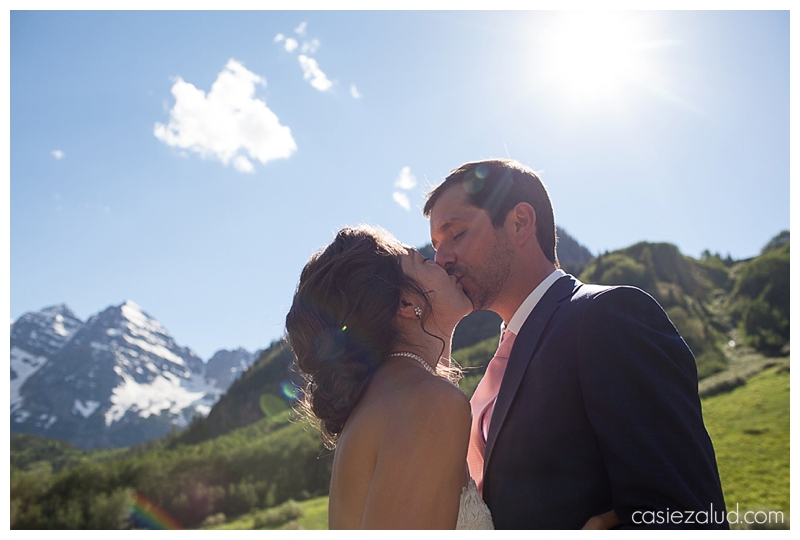 bride and groom kissing with the Maroon Bells behind them and shooting into the sky with sunflare behind them