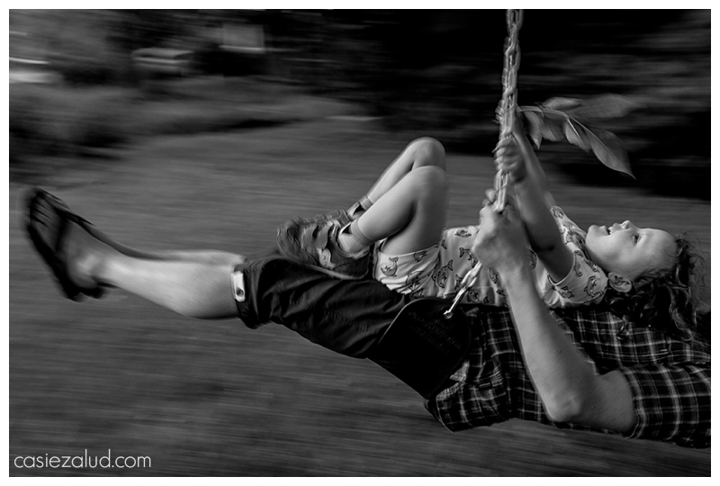 A young girl in motion on her dad's lap swinging from a tree