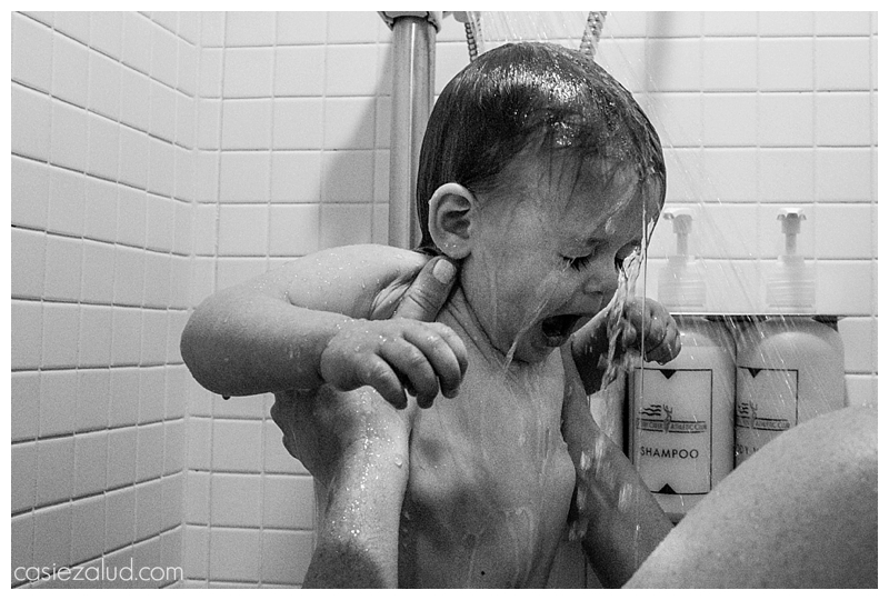 Toddler being help under a shower and not loving it