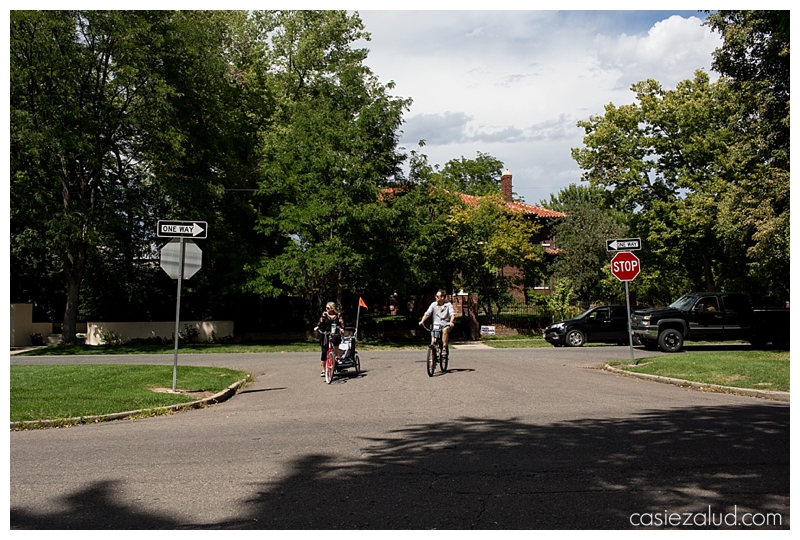 Mom and dad on bikes, mom with a Chariot, waiting at a stop sign, looking for traffic. 