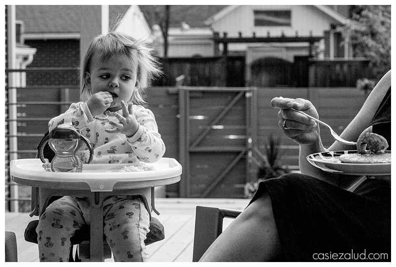 Toddler in her highchair looking longingly at her mother's bite of pancake