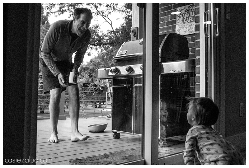 Dad looking through a glass door at a crawling toddler who is laughing her head off