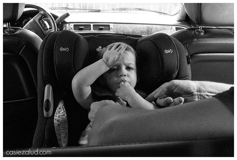 Toddler getting buckled a car seat with her hand on her forehand in a state of exhaustion