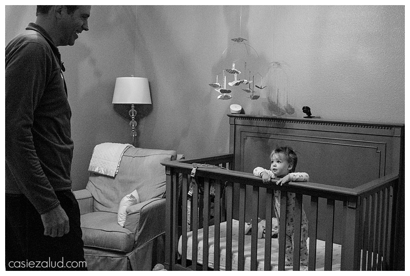 A toddler standing in her crib peering up over the edge at her father.