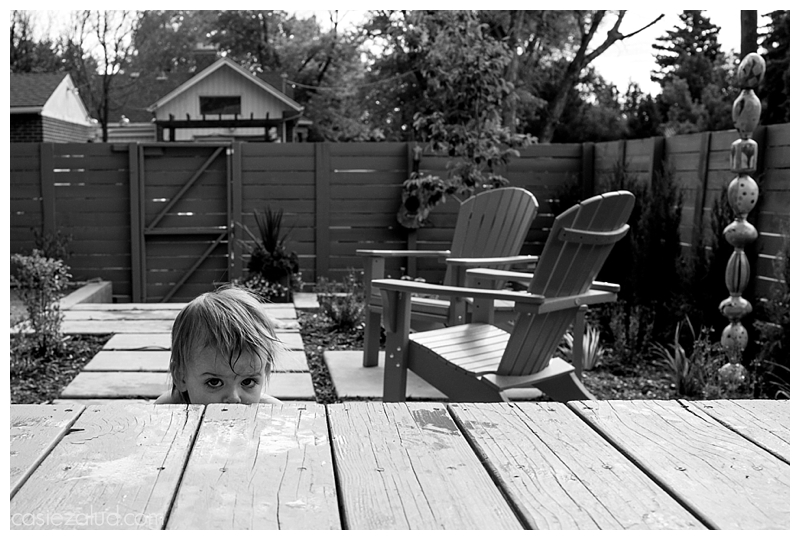 Toddler hiding on a step on the porch so you only see her eyes and the top of her head