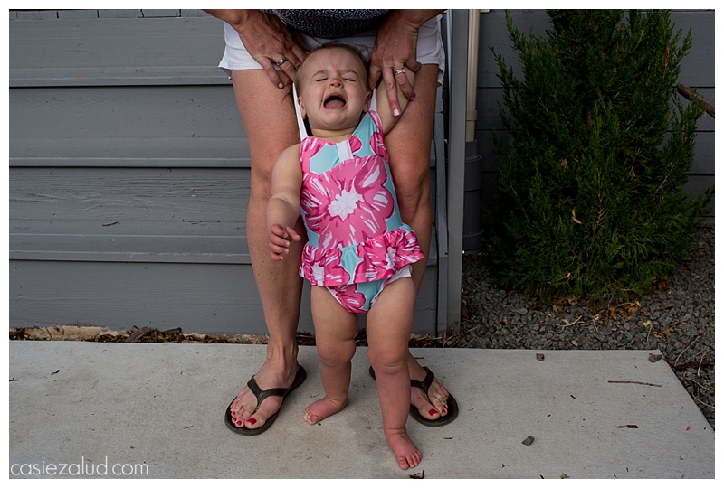 Mom pulling bathing suit straps over the head of a toddler as she screams