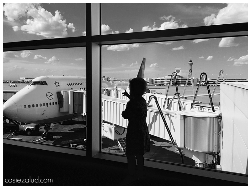 silhouette of a toddler looking out the window at a plane at the airport