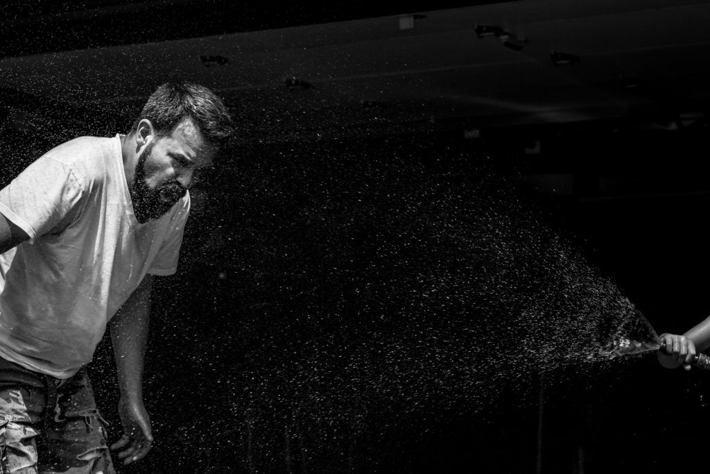 black and white image of son spraying dad with hose in the sunshine and dad cringing