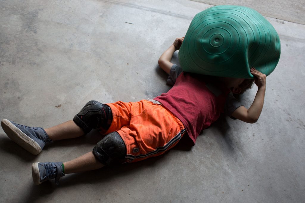 little boy laying on ground with delated exercise ball over his head during a family photography session