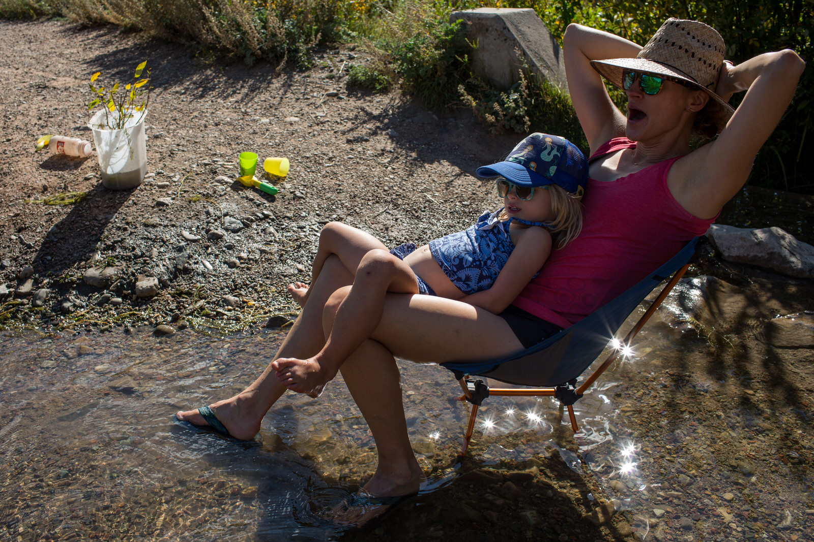 mom sitting in lawn chair in a creek with child on her lap
